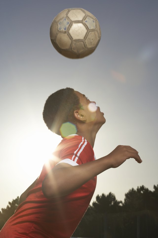 Boy (12-13) heading football, lens flare