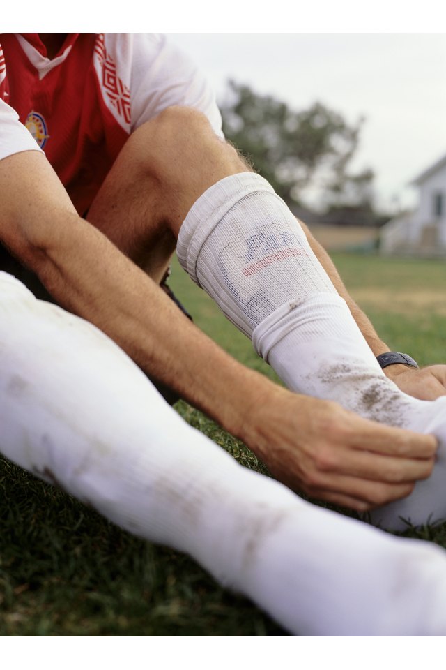 Footballer on pitch adjusting socks, low section, low angle view