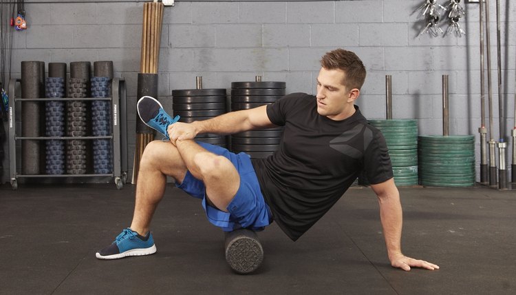 Fit blonde kneeling on floor using foam roller