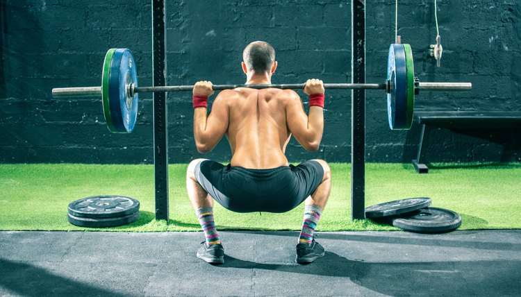 Back view of young sportsman lifting a barbell at the gym