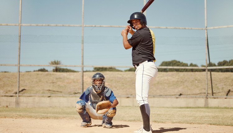 Baseball, pitcher and man with a bat on pitch playing a match or sport training as a team. Fitness, sports and men athletes practicing pitching and batting before a softball game on an outdoor field.