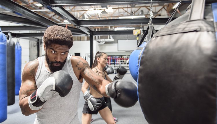 Man and women wearing boxing gloves hitting heavy bags