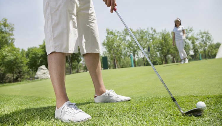 Low section of young man hitting the ball on the golf course, woman in the background