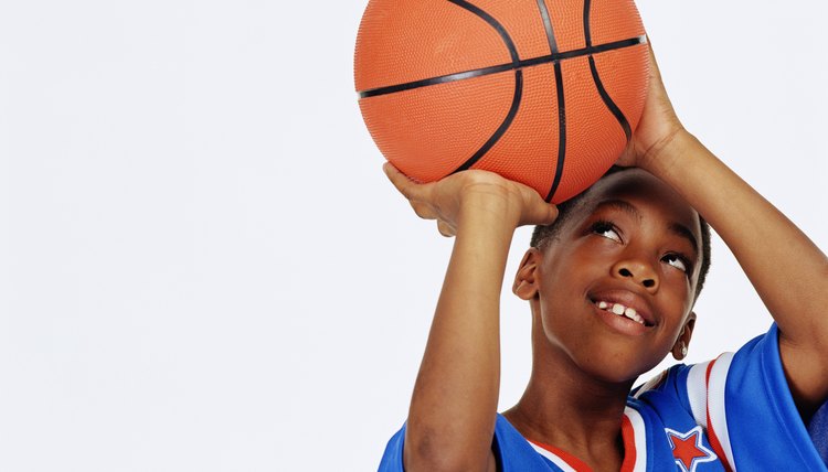 Boy (9-12) looking up aiming basketball, smiling