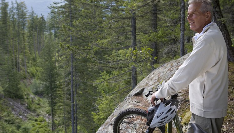 Senior man in mountains standing with bike, looking at view