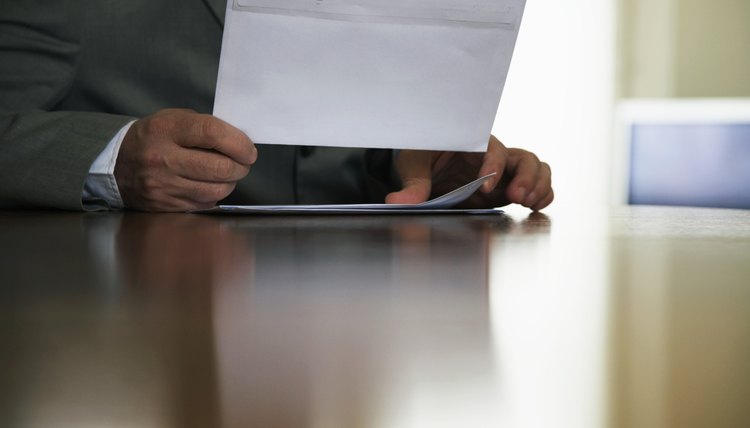 Man sitting at desk holding letter, mid section