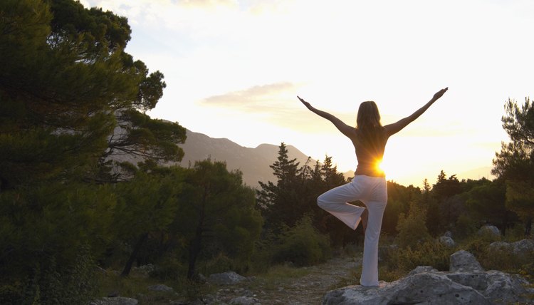 Young woman balancing on rock, practicing yoga pose, rear view