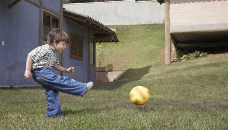 Boy (3-5) playing soccer on lawn, side view