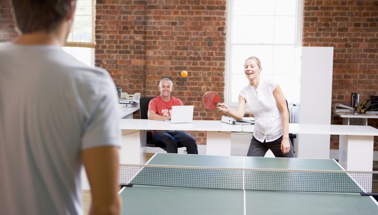 Man and woman in office space playing ping pong