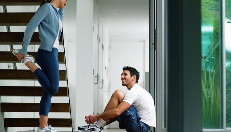 Couple wearing sports clothes in house, woman performing leg stretch
